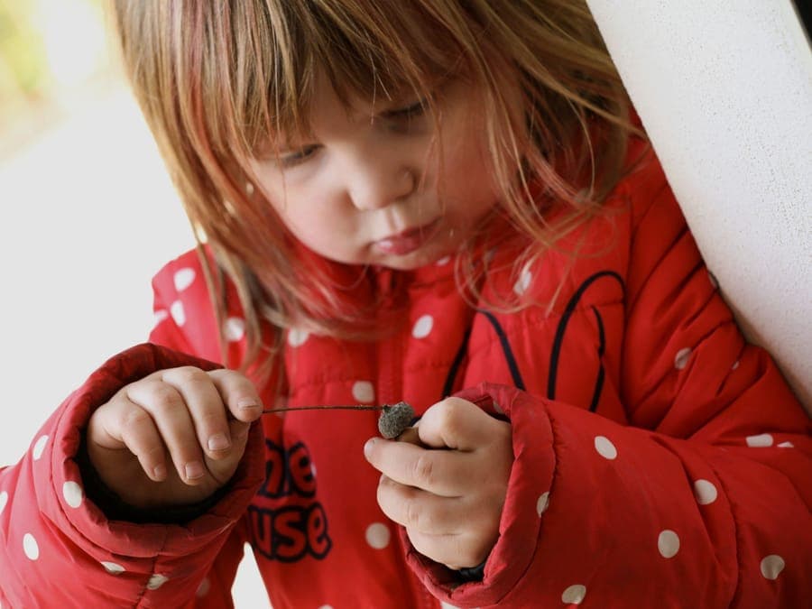 FitKids Kinderkrippe: Kind im gelben Regenanzug geht mit Erzieherin die Gartentreppe hinauf