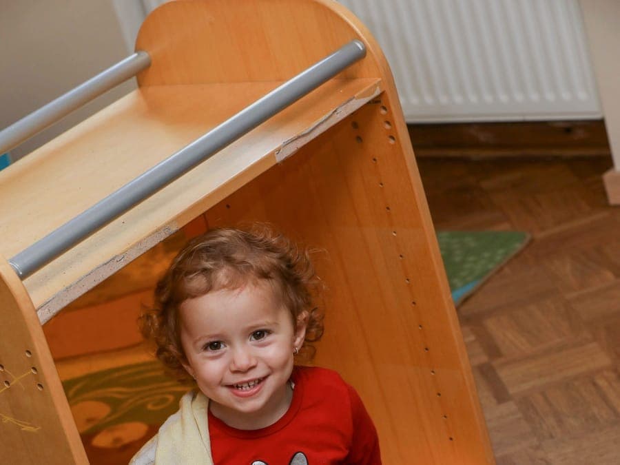 FitKids Krippe: Kleinkind lugt lachend aus der Spielecke hervor