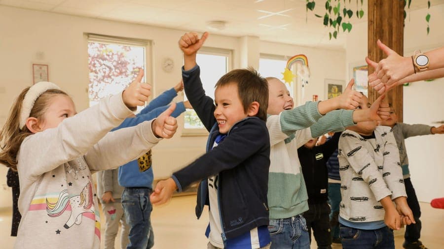 FitClass Grundschulbetreuung: Grundschulkinder im Bewegungsraum zeigen fröhlich Daumen hoch