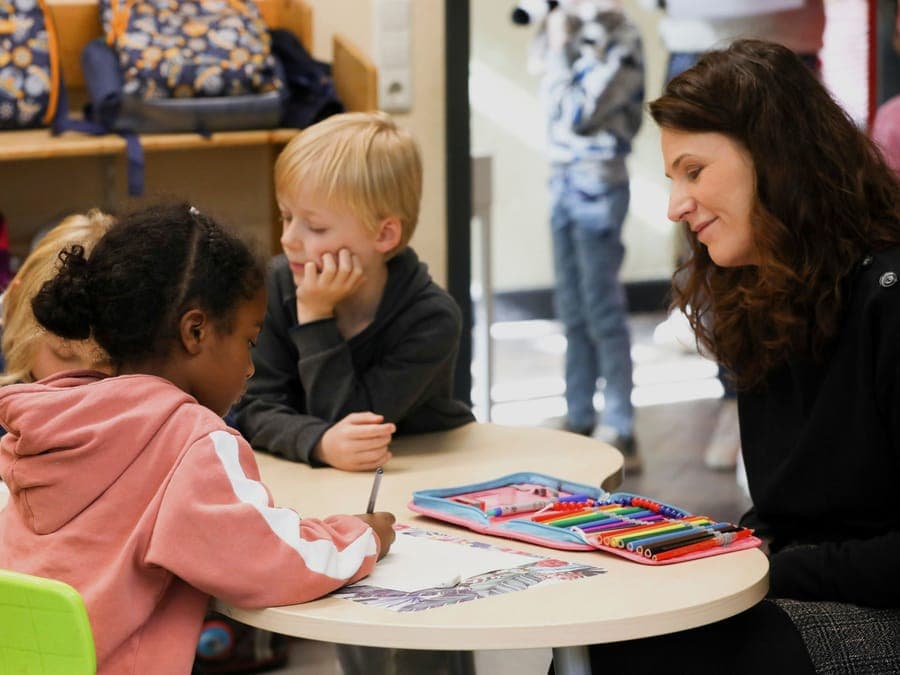 FitClass Schulbetreuung: Betreuerin lächelt mit Schulkindern am Maltisch