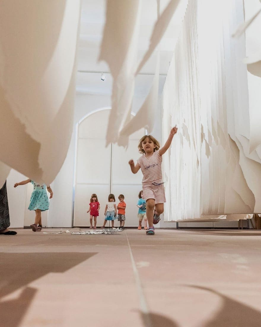 Mädchen läuft freudig durch eine Papier-Kunstinstallation — kreative Projekte bei Fit for Family Care