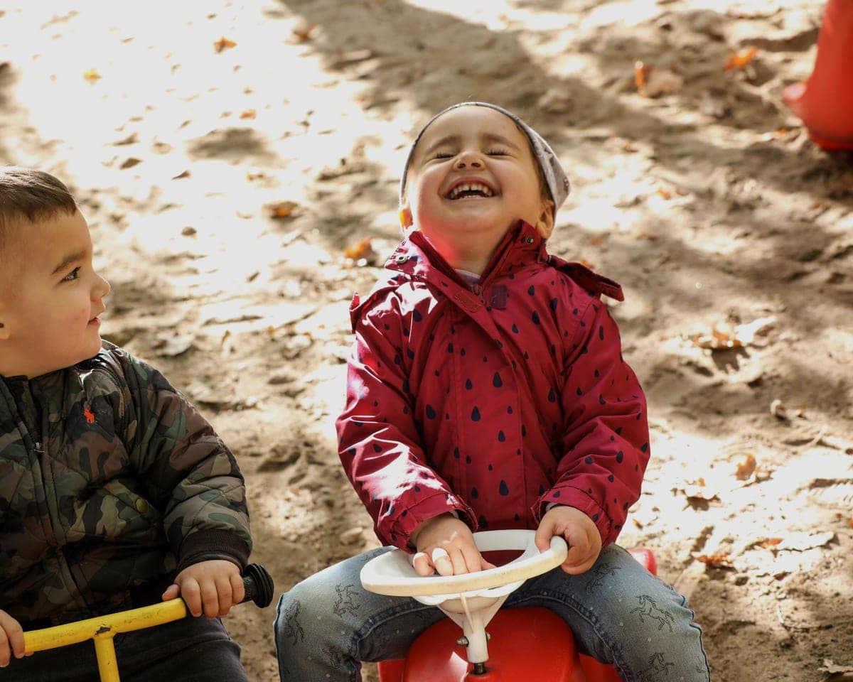FitKids-Krippe Wiesbaden: zwei Kleinkinder auf Bobbycar und Hüpftier, eines lacht herzhaft