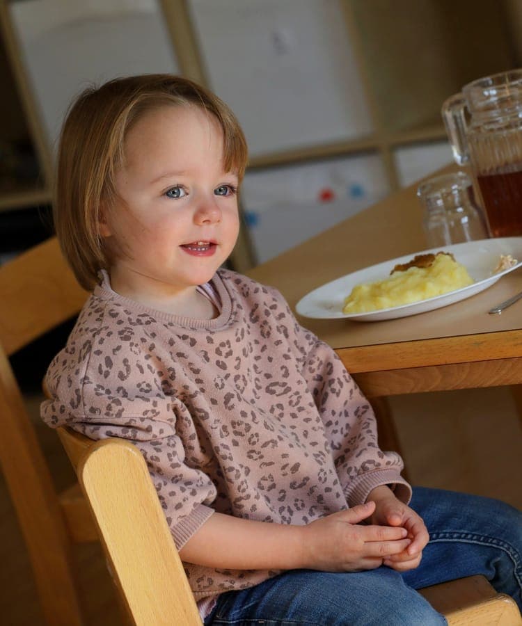 FitKids Krippe: Kleinkind sitzt entspannt beim gemeinsamen Mittagessen