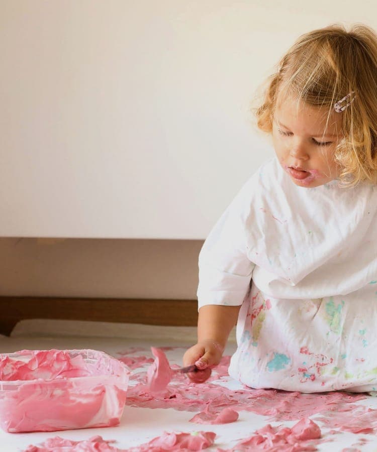 FitKids Krippe: Kleinkind malt kniend und vertieft mit Fingerfarbe