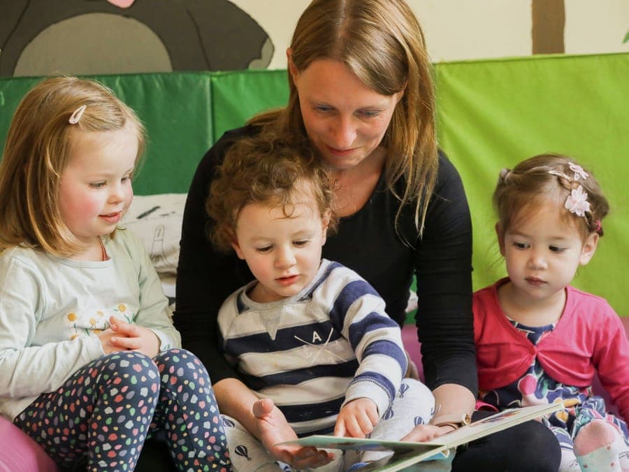 Fit for Family Care Krippe: Erzieherin schaut mit Kleinkindern ein Bilderbuch an