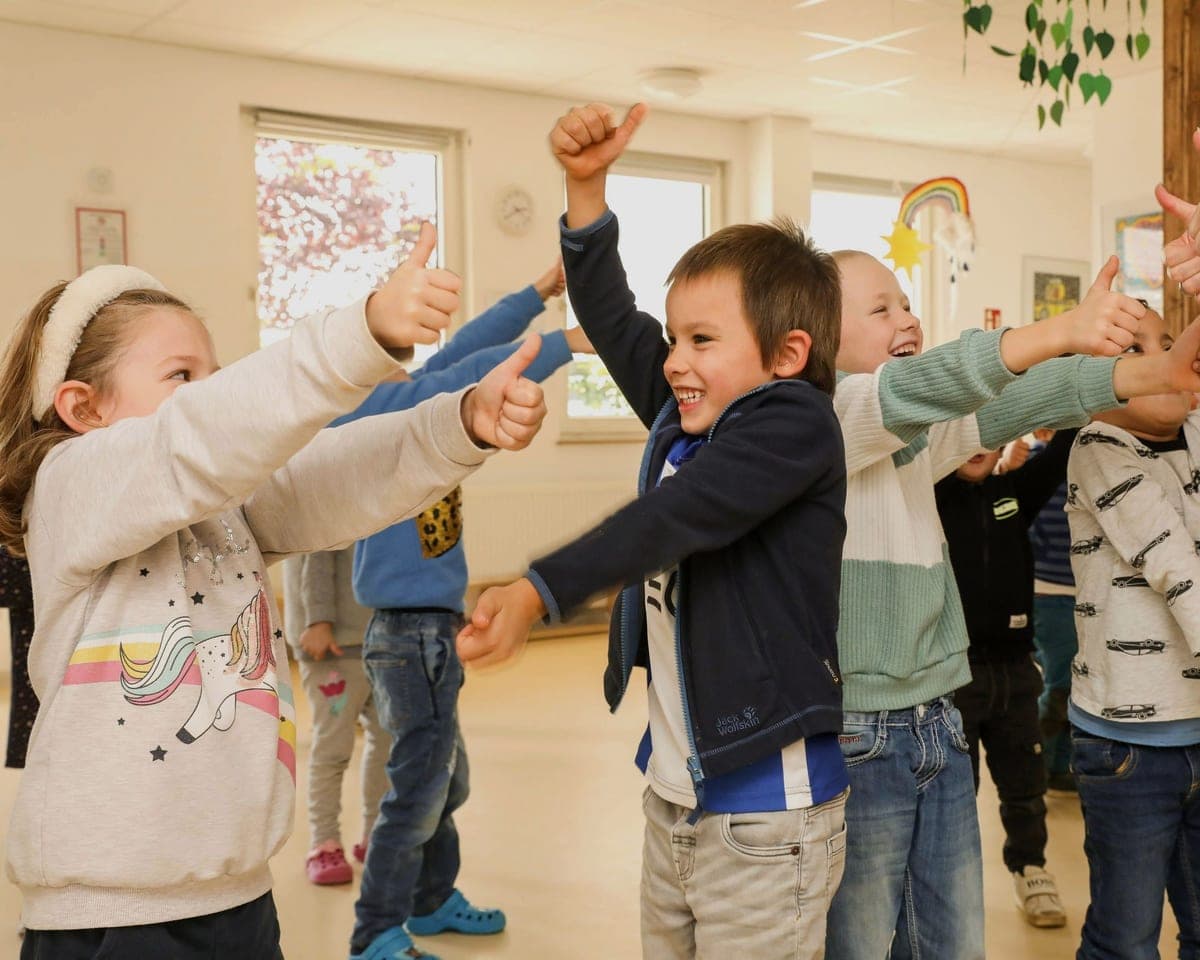 FitClass Grundschulbetreuung Wiesbaden: fröhliche Grundschulkinder im Bewegungsraum zeigen Daumen hoch