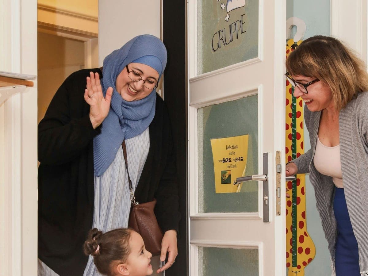Kind wird in der Kita von einer Erzieherin begrüßt: Anmeldung und Betreuungsplatz bei Fit for Family Care