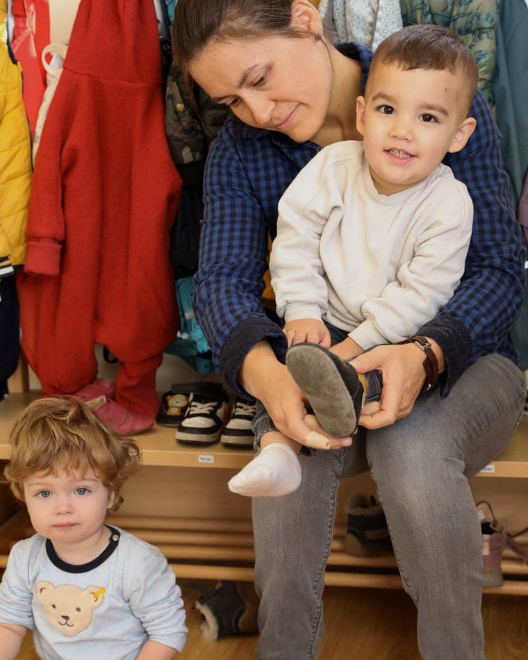 Erzieherin zieht einem Kind in der Garderobe einer FFF-Einrichtung herzlich die Schuhe an