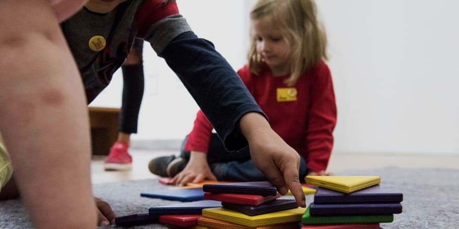 Kinderhände stapeln farbige Legematerial-Plättchen in der Kita