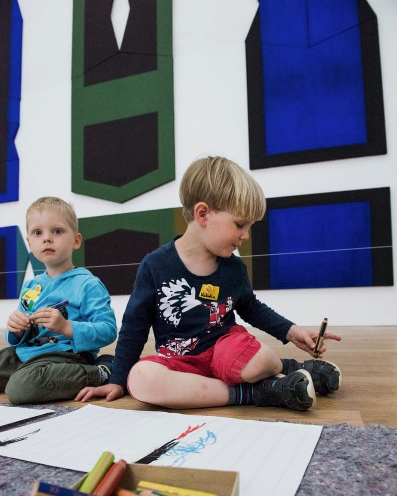 Zwei Jungen zeichnen nebeneinander vor einer Kunstwand in der FFF-Kita