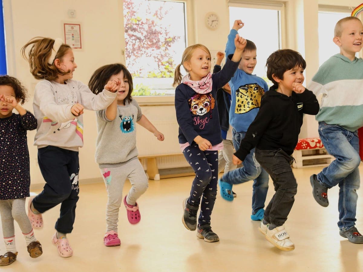 Kindergruppe tanzt fröhlich im Bewegungsraum der Kita