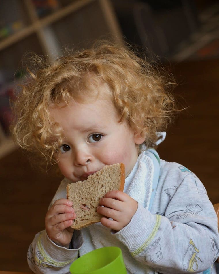Kleinkind isst genüsslich ein Brot in der Kita