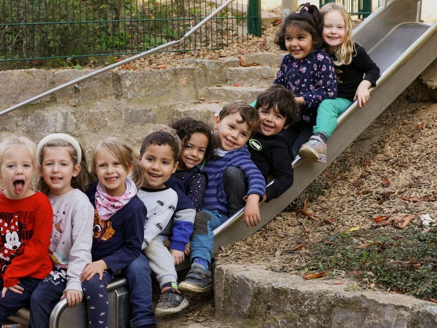 Fröhliche Kindergruppe sitzt dicht beieinander auf einer Rutsche im Außengelände