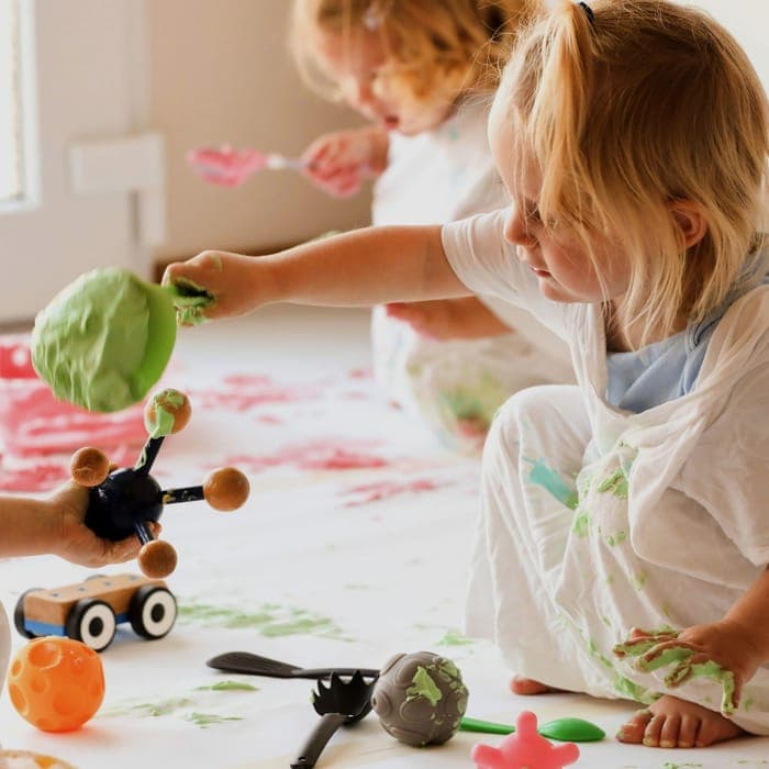 Kleinkinder beim Fingermalen mit bunten Farben am Boden