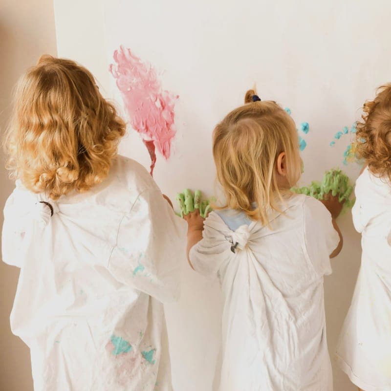 Vier Kinder malen gemeinsam an einer weißen Wand im Kita-Alltag Wiesbaden
