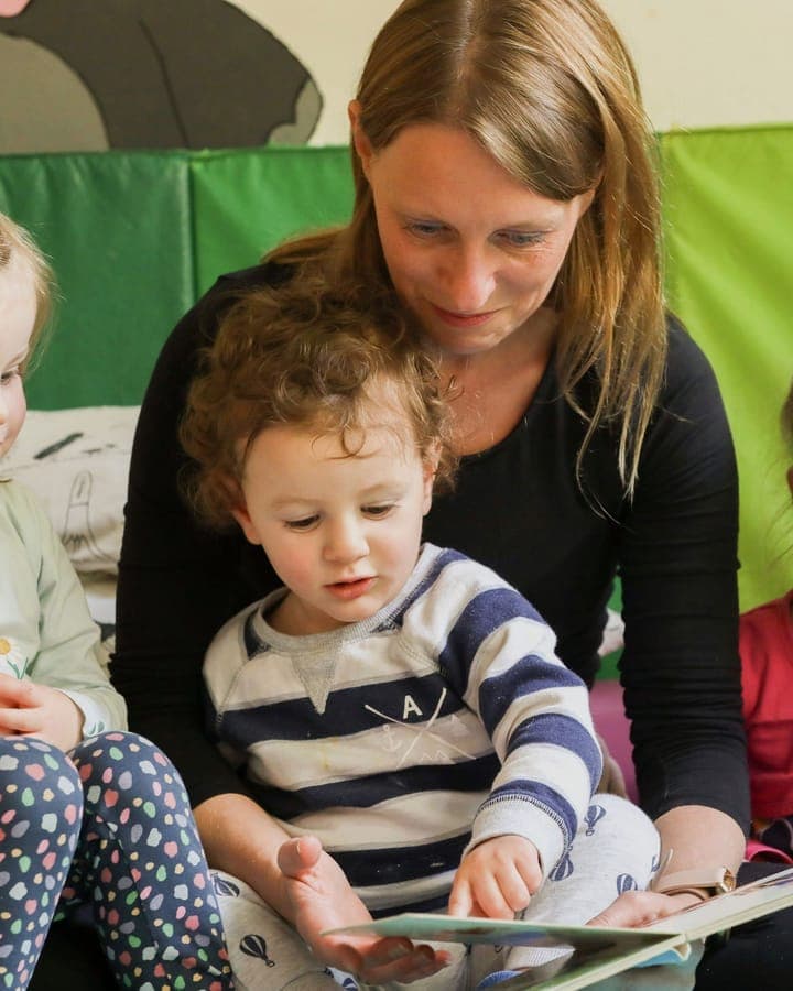 Erzieherin schaut gemeinsam mit Kleinkindern ein Bilderbuch an